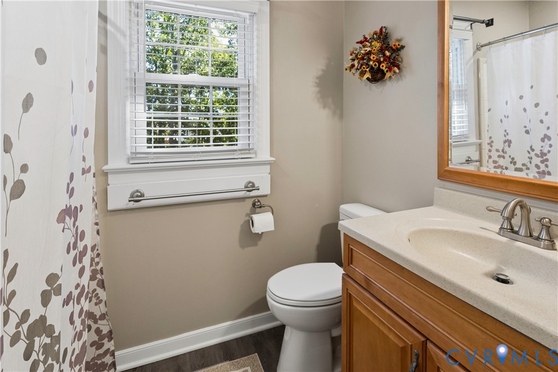 Bathroom featuring a wood-toned vanity with an integrated solid surface countertop, dual-handle metal faucet, framed wall mirror, and a window with horizontal blinds