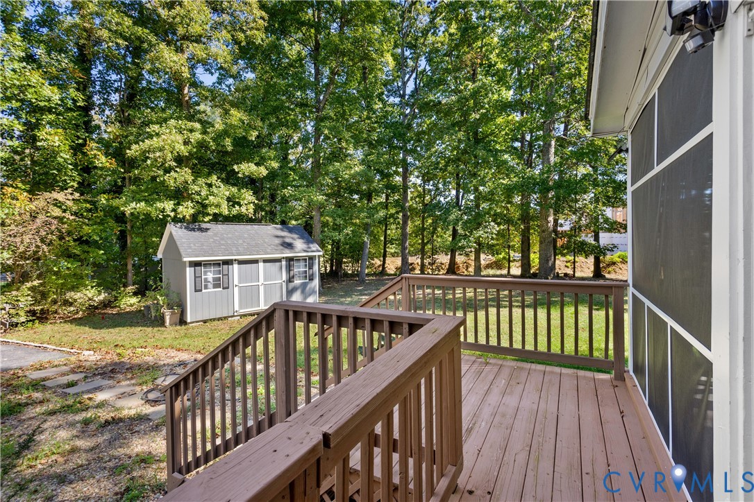 Elevated wooden deck with balustrades, screened enclosure, detached storage shed, and mature tree-lined perimeter