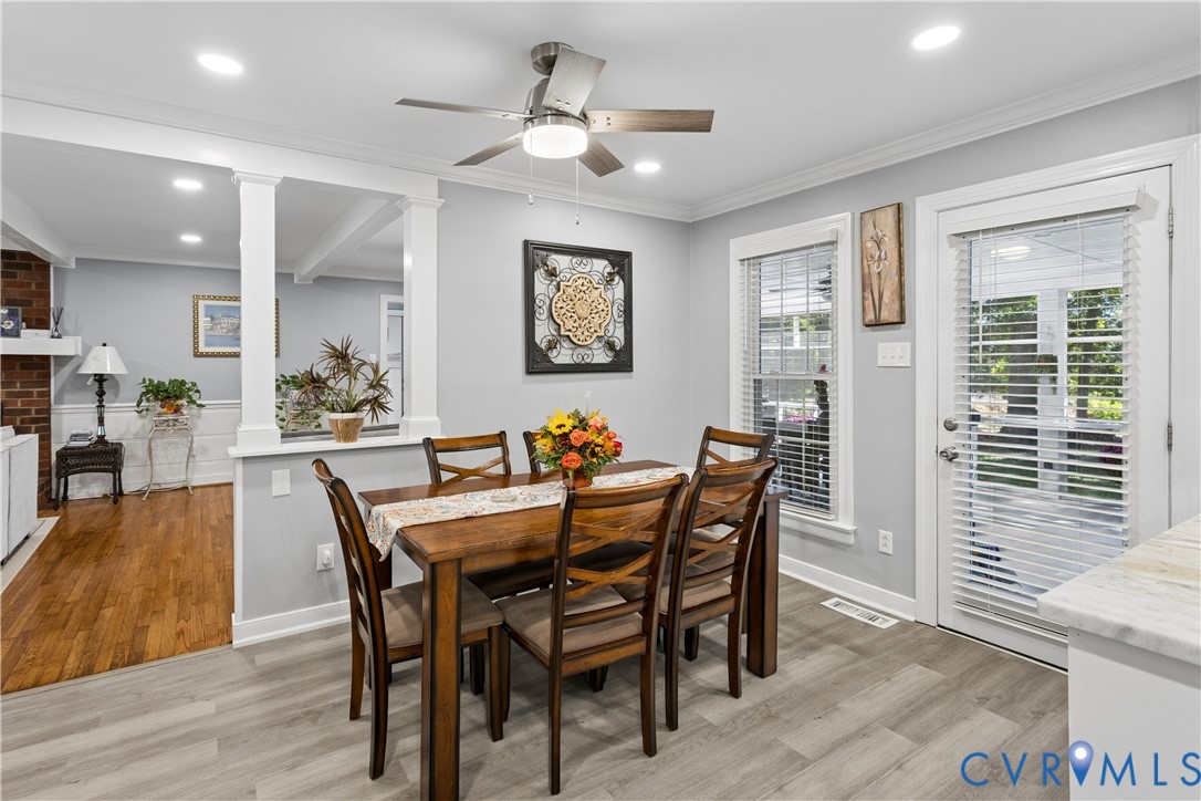 Open-concept interior featuring wood-finish flooring, a contemporary ceiling fan with integrated lighting, recessed lighting, half-wall partition with structural columns, and a glass-paneled exterior door