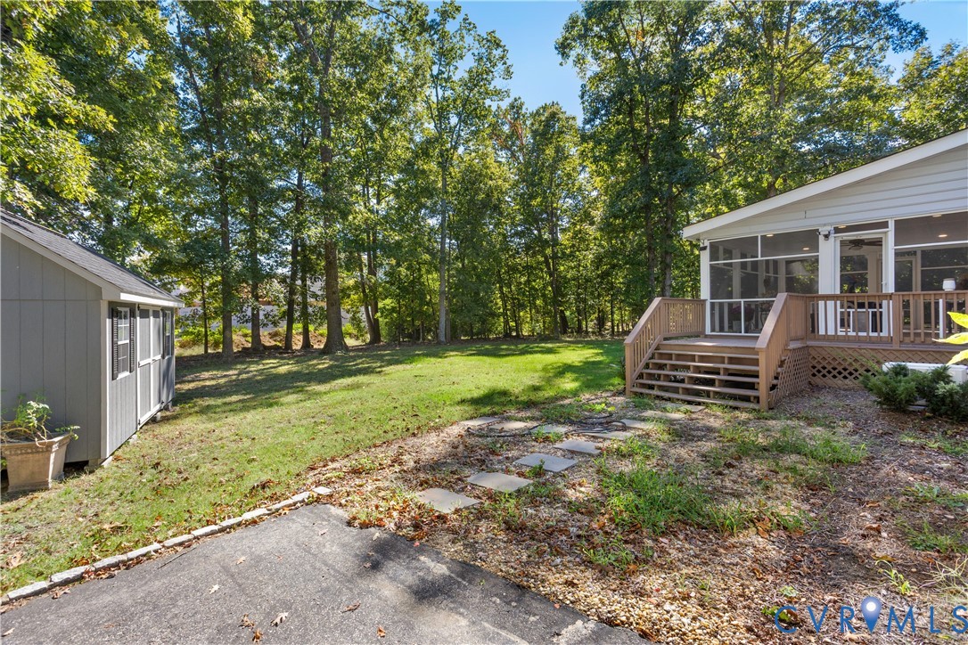 Rear exterior featuring a screened-in porch with wood-tone decking, a detached storage shed, stepping stone path, and a grass-covered backyard framed by mature trees