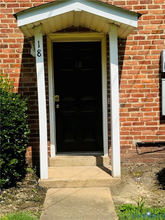 Exterior entry featuring a red brick facade, a covered portico with dual white support columns, and a solid black entry door Exterior entry featuring a red brick facade, a covered portico with dual white support columns, and a solid black entry door