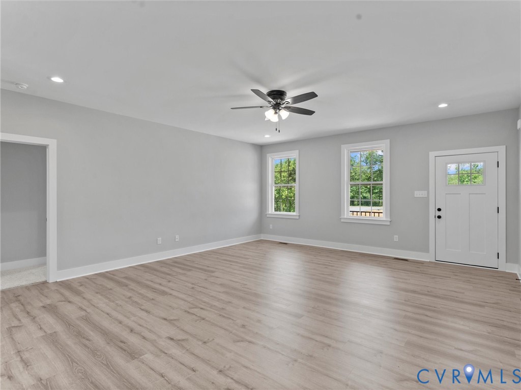 Open-concept interior featuring wood-finish flooring, recessed lighting, a central ceiling fan with integrated light fixture, two double-pane windows, and an exterior door with a glass pane