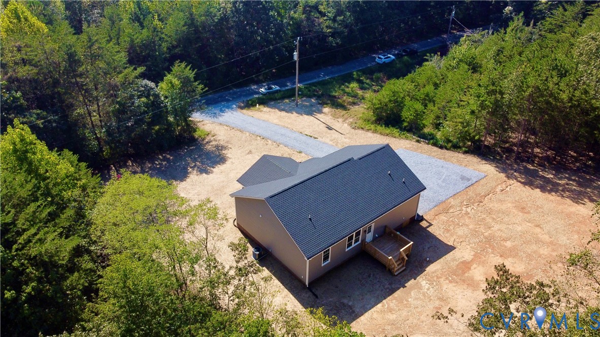 Gabled roof structure with dark shingling, elevated wooden deck, and gravel driveway situated on a wooded lot