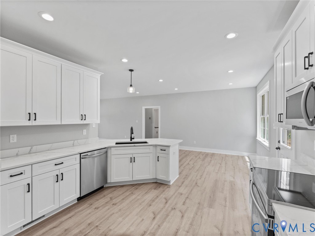 Kitchen featuring white shaker-style cabinetry, solid-surface countertops, wood-finish flooring, stainless steel appliances, and recessed lighting