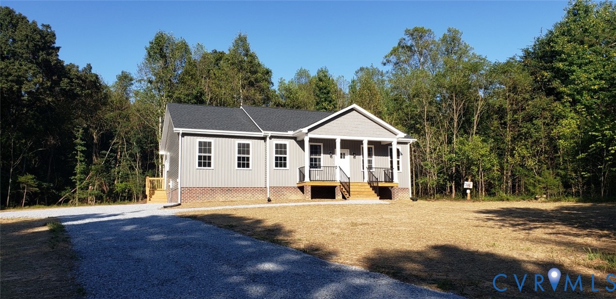 Single-story residence featuring vertical siding, a brick foundation, a covered front porch with metal railing, and a gravel driveway
