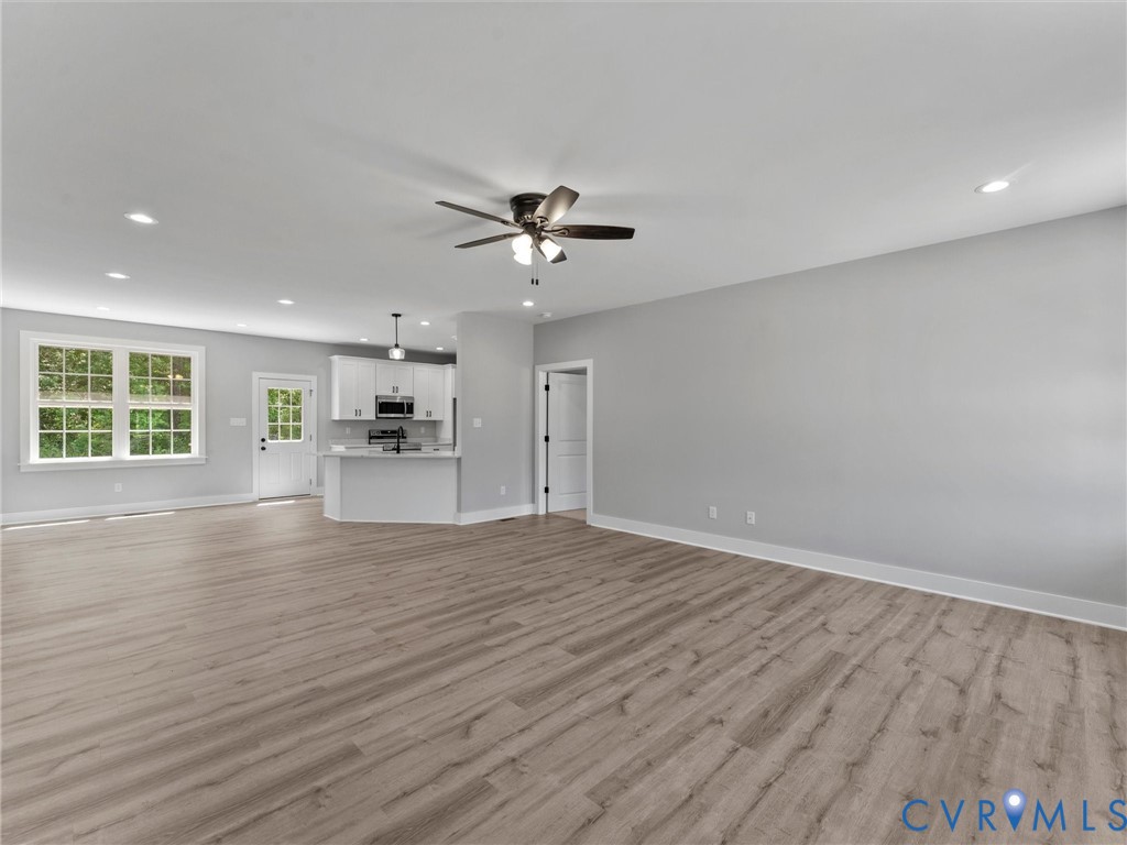Wood-finish flooring, recessed lighting, ceiling fan, white cabinetry, and multi-pane window