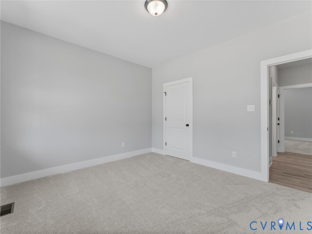 Neutral-toned interior room featuring wall-to-wall carpeting, a two-panel interior door, and a central flush-mount ceiling light fixture