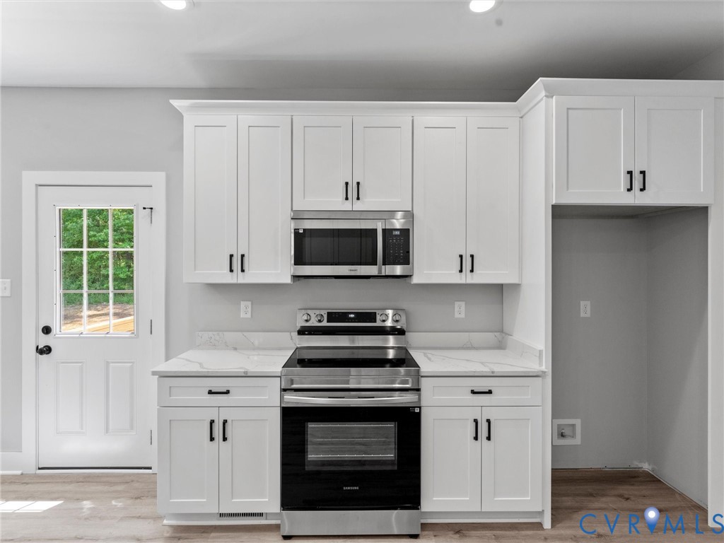 White Shaker-style cabinetry, stone-finish countertops, stainless steel appliances, and wood-finish flooring, featuring a single-light exterior door