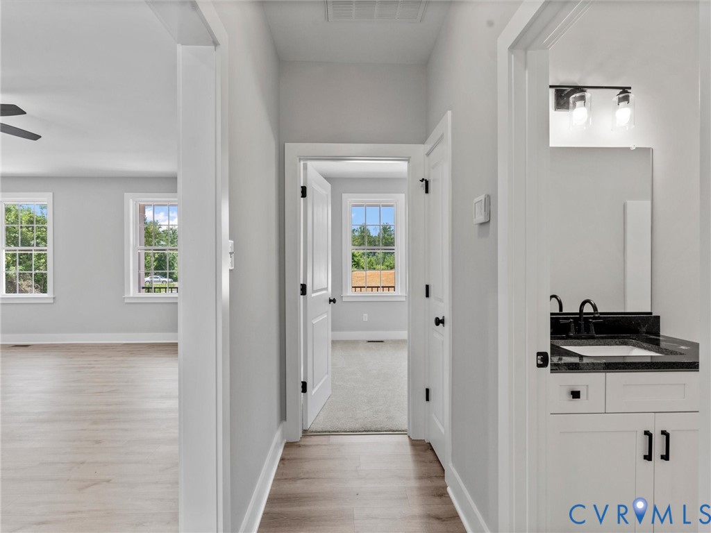 Neutral interior hallway featuring wood-finish flooring, white shaker-style cabinetry with dark hardware, stone-top vanity, and dual-light wall sconce