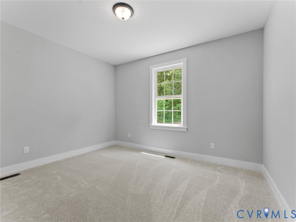 Neutral-toned room featuring wall-to-wall carpeting, a single double-hung window with muntins, and a flush-mount ceiling light fixture