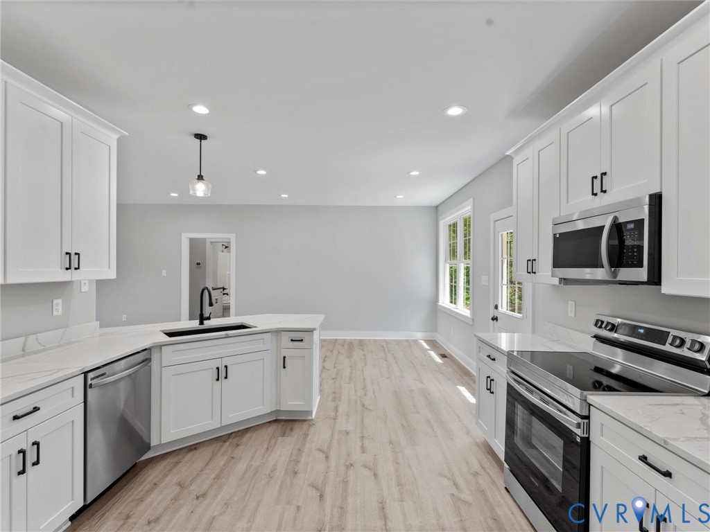 Kitchen featuring white shaker-style cabinetry, stainless steel appliances, light-toned wood-finish flooring, recessed lighting, and stone-surface countertops