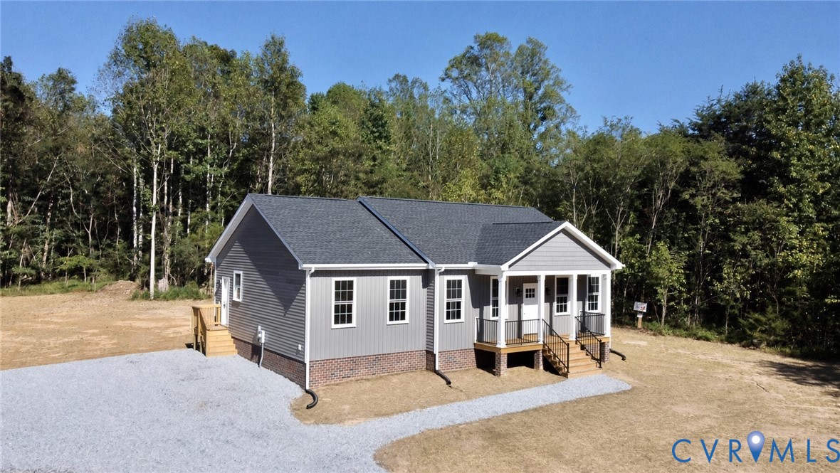 Single-story residence featuring horizontal and vertical siding, a brick foundation, a covered front porch, and a gravel driveway