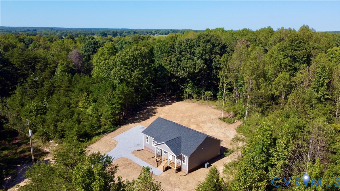 Aerial perspective of a detached residential structure featuring a gable roof, concrete driveway, and covered front entry, set on a sprawling parcel surrounded by mature woodland