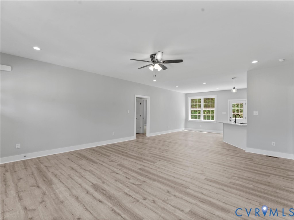 Spacious room featuring wood-finish flooring, recessed lighting, a ceiling fan with integrated lighting, a multi-pane window, and a breakfast bar with pendant lighting
