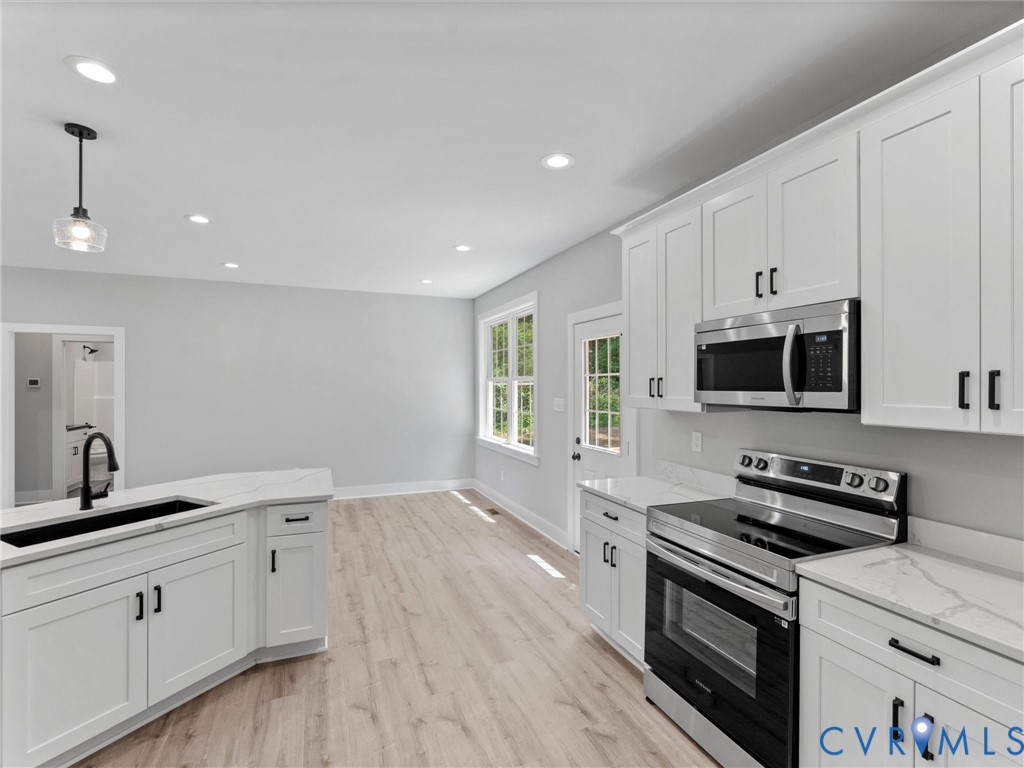 Kitchen featuring white shaker-style cabinetry, stainless steel appliances, quartz countertops, a dual-basin sink with a matte black faucet, and wood-finish flooring