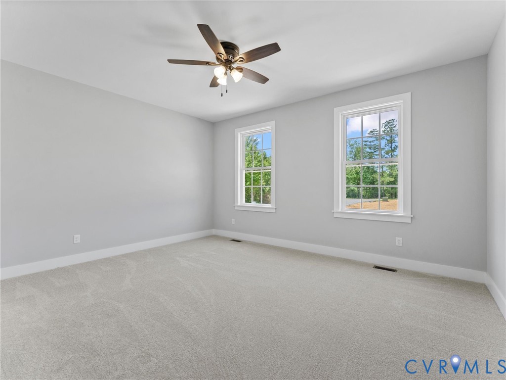 Room featuring neutral-toned carpeting, two double-hung windows, and a multi-blade ceiling fan with an integrated light fixture