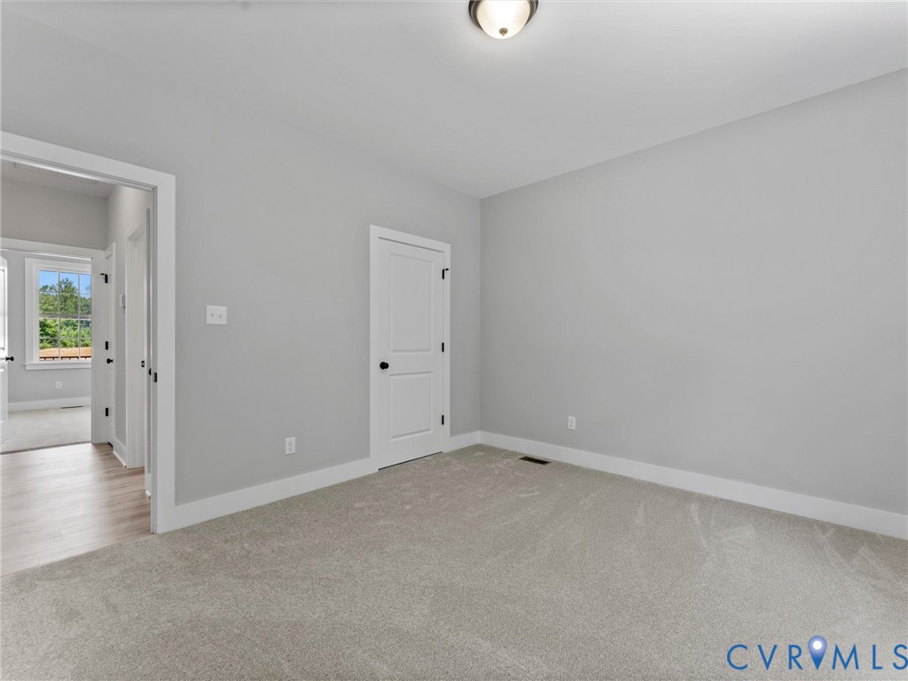 Neutral-toned interior room featuring wall-to-wall carpeting, two-panel interior doors with matte black hardware, and a flush-mount ceiling light fixture
