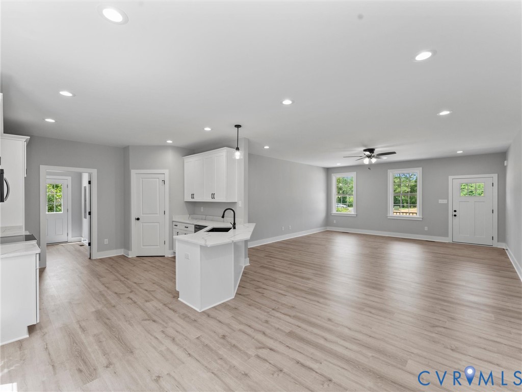 Open-concept interior featuring light-toned wood-finish flooring, recessed lighting, white cabinetry, a kitchen island with a dark faucet, and multi-pane exterior doors