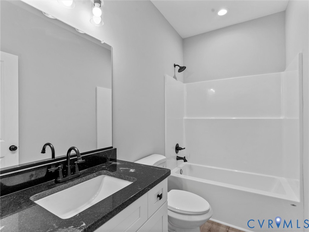 Bathroom featuring a white vanity with a dark stone countertop, undermount sink, large wall-mounted mirror, and matte black fixtures throughout, including a tub-shower combination