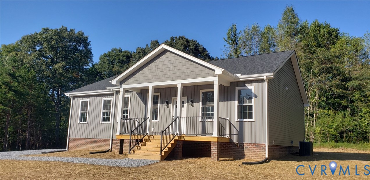 Single-story exterior featuring gray vertical siding, a brick foundation, a covered front porch with wood decking, and black metal railings
