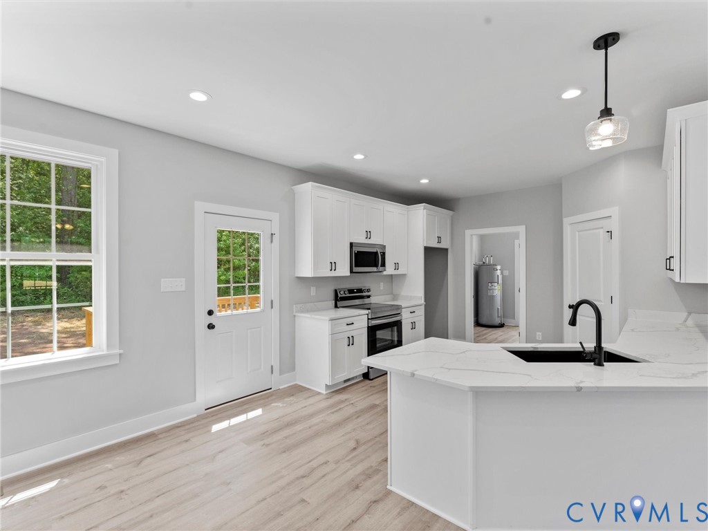 Kitchen featuring white cabinetry, light-toned wood-finish flooring, stone-finish countertops with veining, an undermount sink with a matte black faucet, and recessed lighting