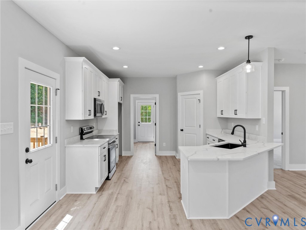 Kitchen featuring white cabinetry, quartz countertops, a peninsula with an undermount sink, matte black fixtures, and wood-finish flooring