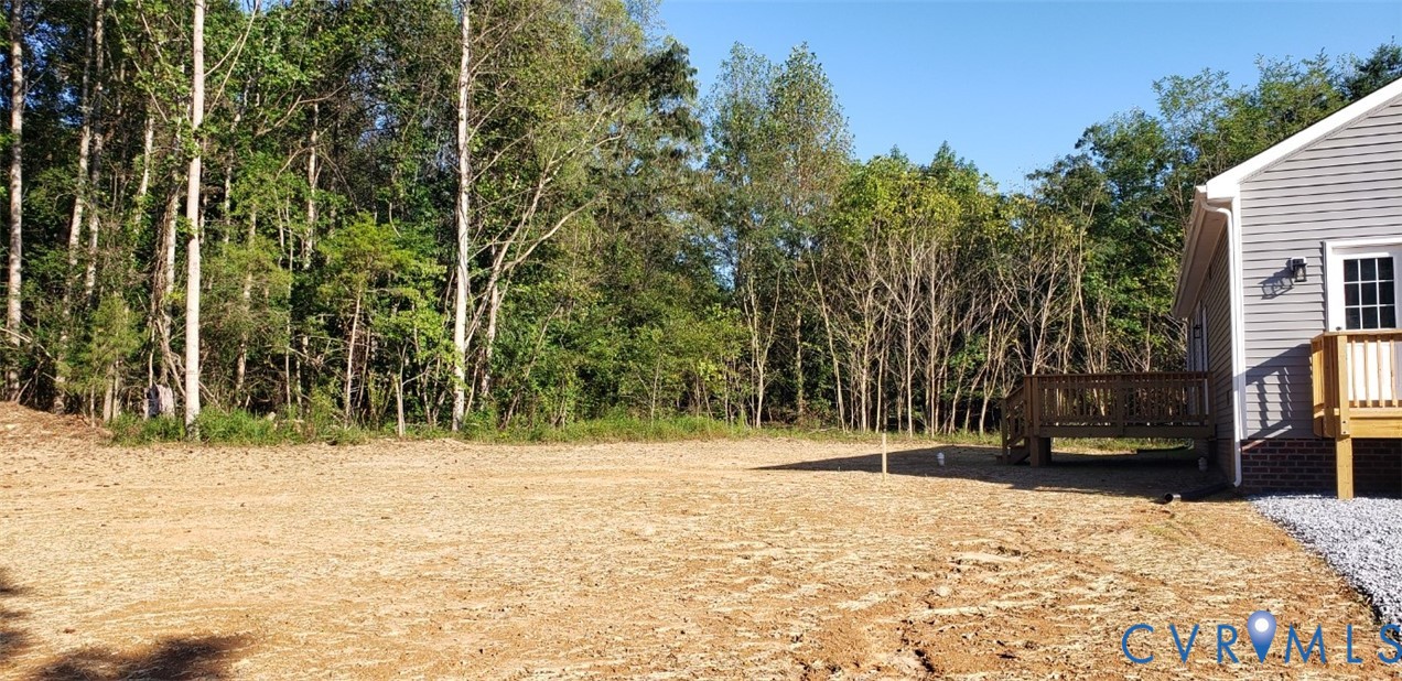 Expansive backyard featuring cleared level terrain, a wood deck, and mature woodland borders