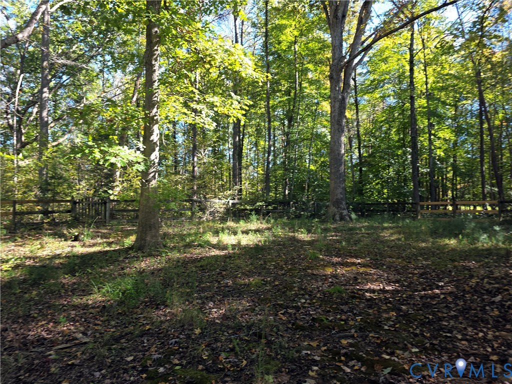 Wooded backyard area featuring a post-and-rail perimeter fence and mature trees