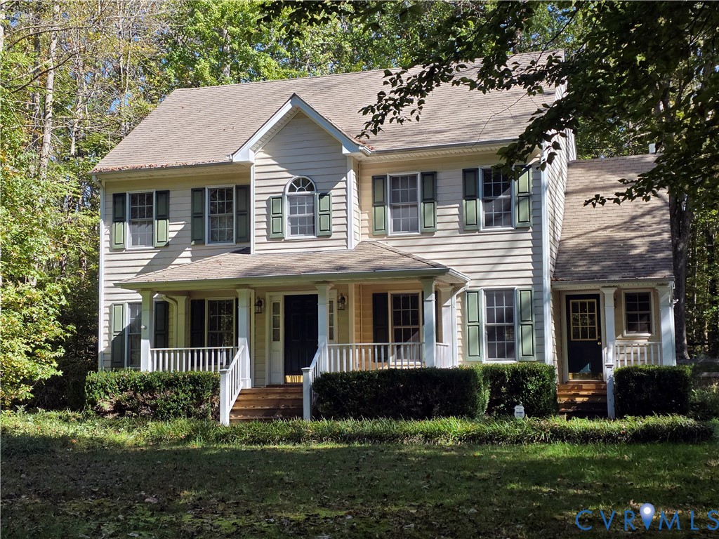 Two-story colonial residence featuring horizontal siding, a covered front porch with white railings, and decorative window shutters