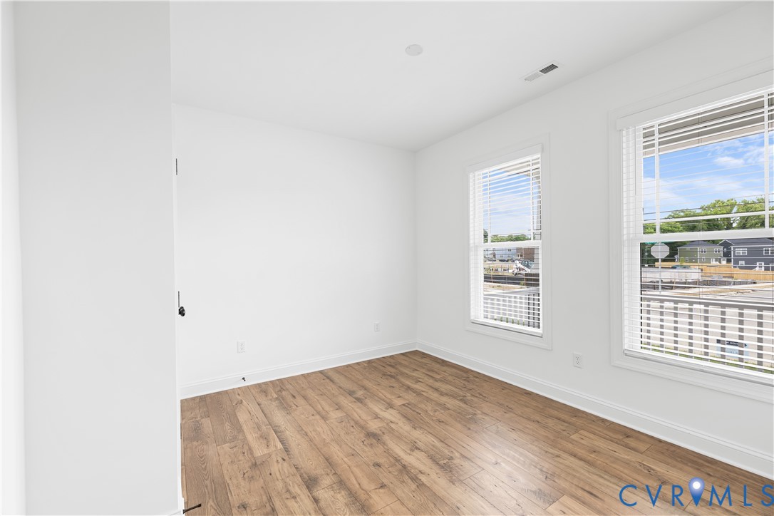 Bright room featuring wood-finish flooring, white walls, and two windows with blinds