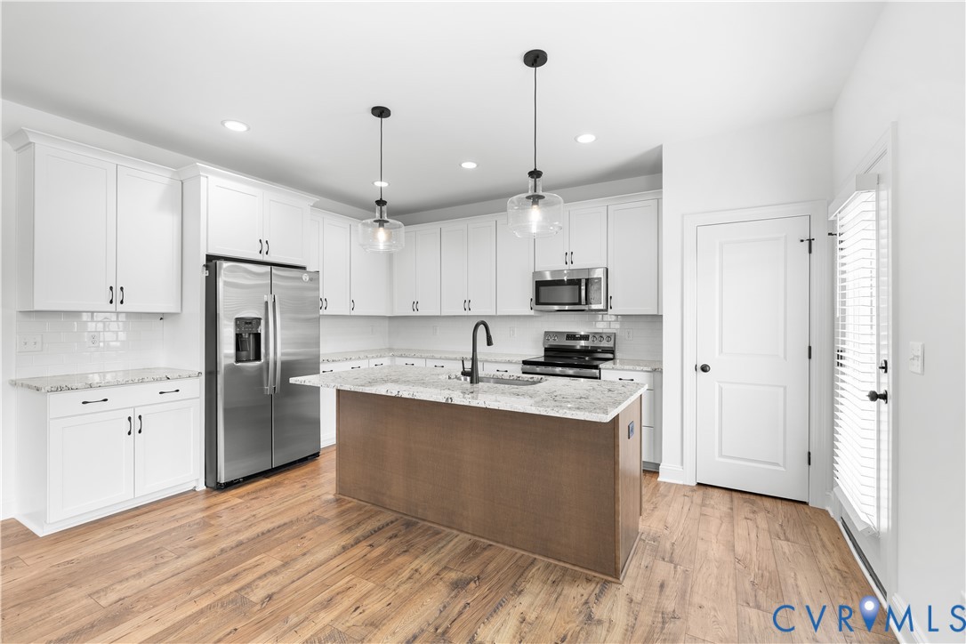 Modern kitchen featuring white shaker cabinetry, stainless steel appliances, a wood-finish island with a stone countertop, and wood-finish flooring