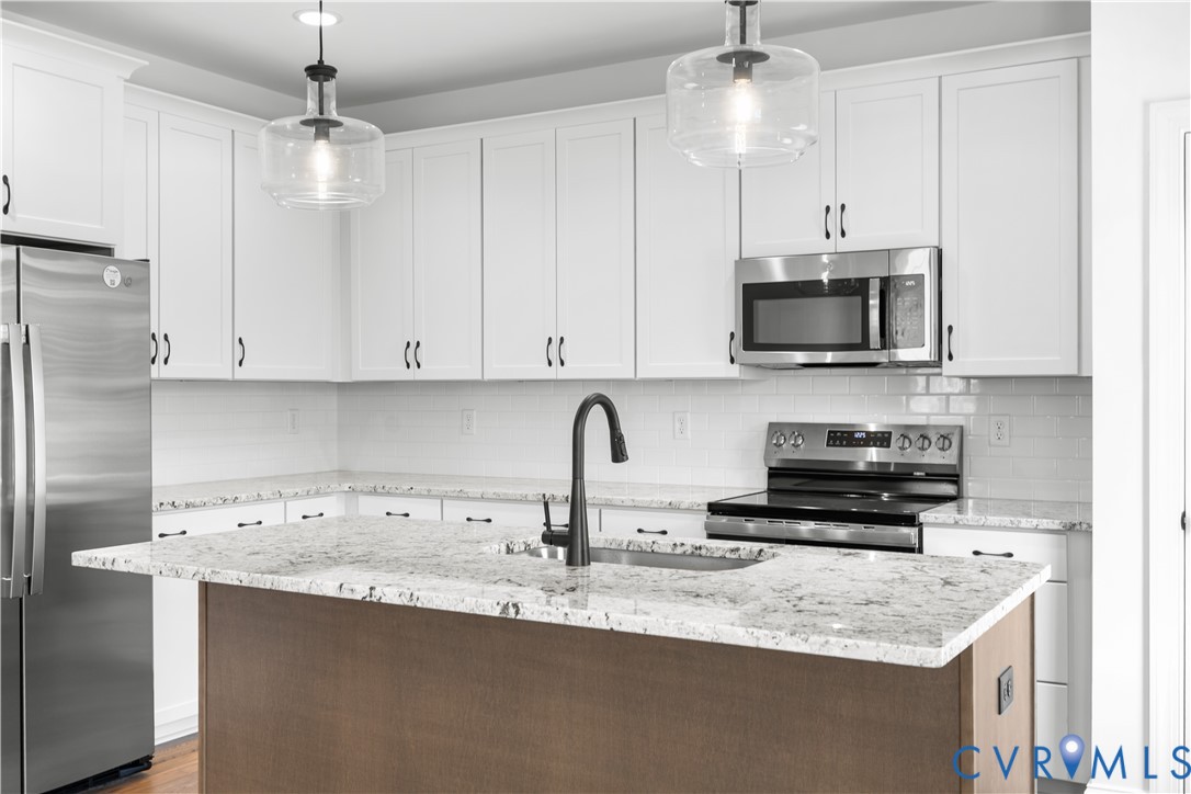 Kitchen featuring white shaker-style cabinetry with dark hardware, stainless steel appliances, and a central island with a wood-finish base and light-toned countertop