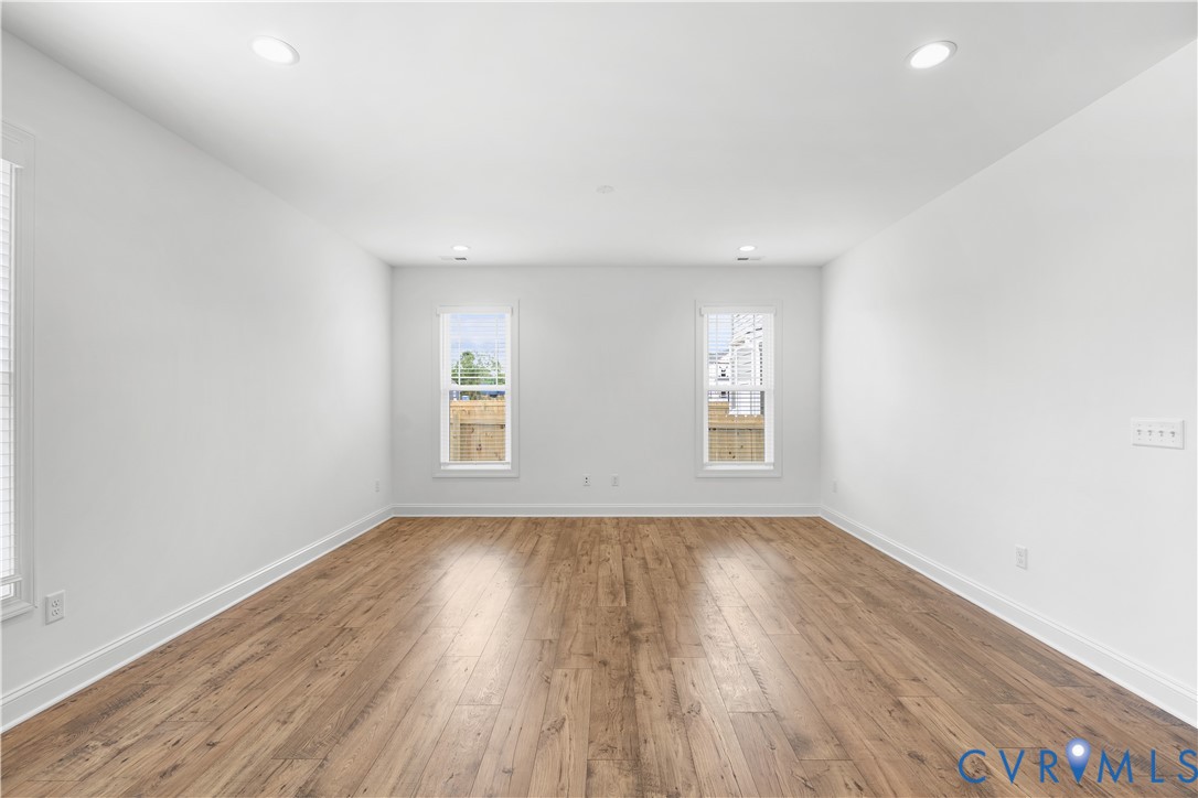 Spacious room featuring wood-finish flooring, white walls, and recessed lighting