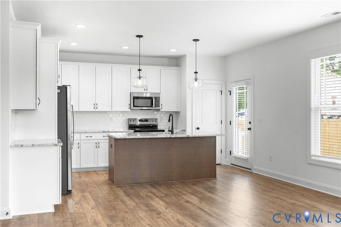 Kitchen featuring white cabinetry, stone countertops, stainless steel appliances, a subway tile backsplash, and a central island with pendant lighting