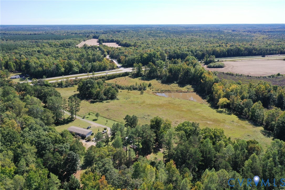 Aerial perspective of a sprawling property featuring expansive open pastureland, a private pond, and established perimeter woodlands Aerial perspective of a sprawling property featuring expansive open pastureland, a private pond, and established perimeter woodlands
