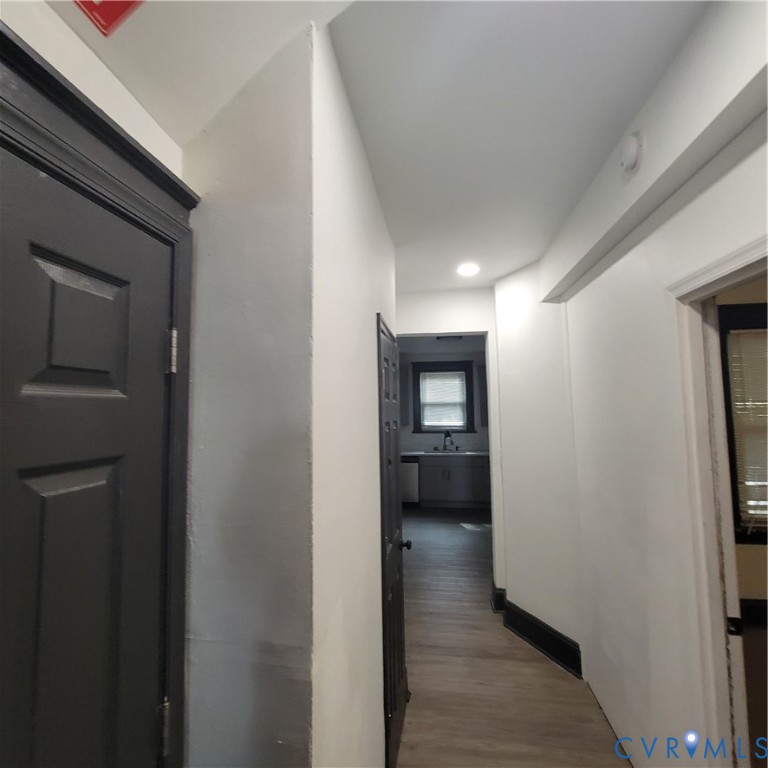 Hallway featuring wood-finish flooring, recessed lighting, and dark-toned interior doors with matching trim