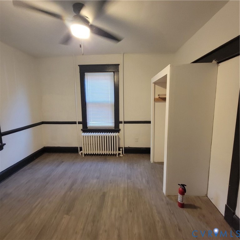 Interior space featuring wood-finish flooring, high-contrast dark trim, a built-in closet, a window with horizontal blinds, and a ceiling-mounted light fixture with fan