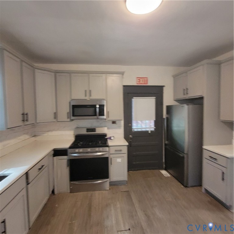 Kitchen featuring light gray cabinetry, stainless steel appliances, solid surface countertops, and wood-finish flooring