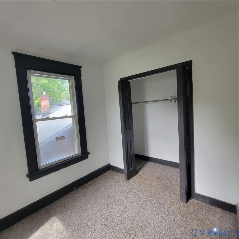 Neutral-toned interior space featuring carpeting, a double-hung window with dark-toned trim, and a built-in closet with folding doors