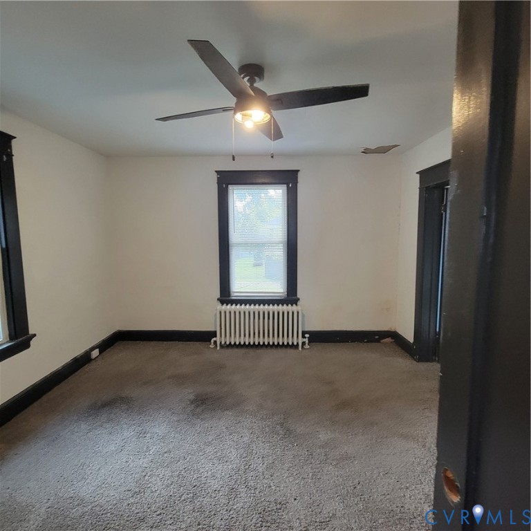 Room featuring dark-finished door and window trim, a multi-blade ceiling fan with integrated lighting, and a white cast-iron radiator