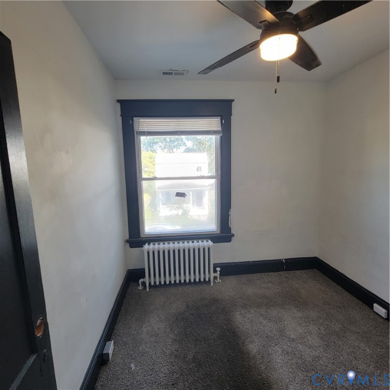 Interior space featuring high-contrast dark trim, wall-to-wall carpeting, a cast-iron radiator, and an integrated ceiling fan with a light fixture