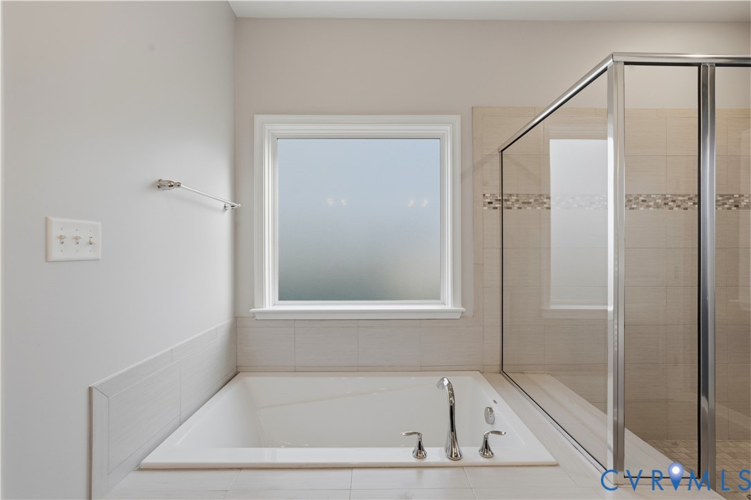 Downstairs Primary bathroom. Built-in soaking tub with chrome fixtures, tiled tub surround, and a glass-enclosed shower with mosaic tile inlay
