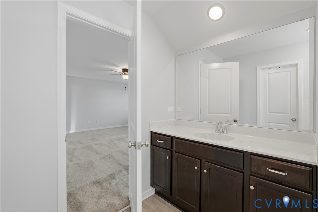 Upstairs Primary Bathroom vanity featuring dark-toned cabinetry, light-toned stone-finish countertop, integrated oval basin, and a large wall-mounted mirror