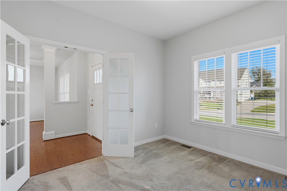 Room featuring glass-paned double doors, neutral-toned wall-to-wall carpeting, and dual-pane windows with horizontal blinds