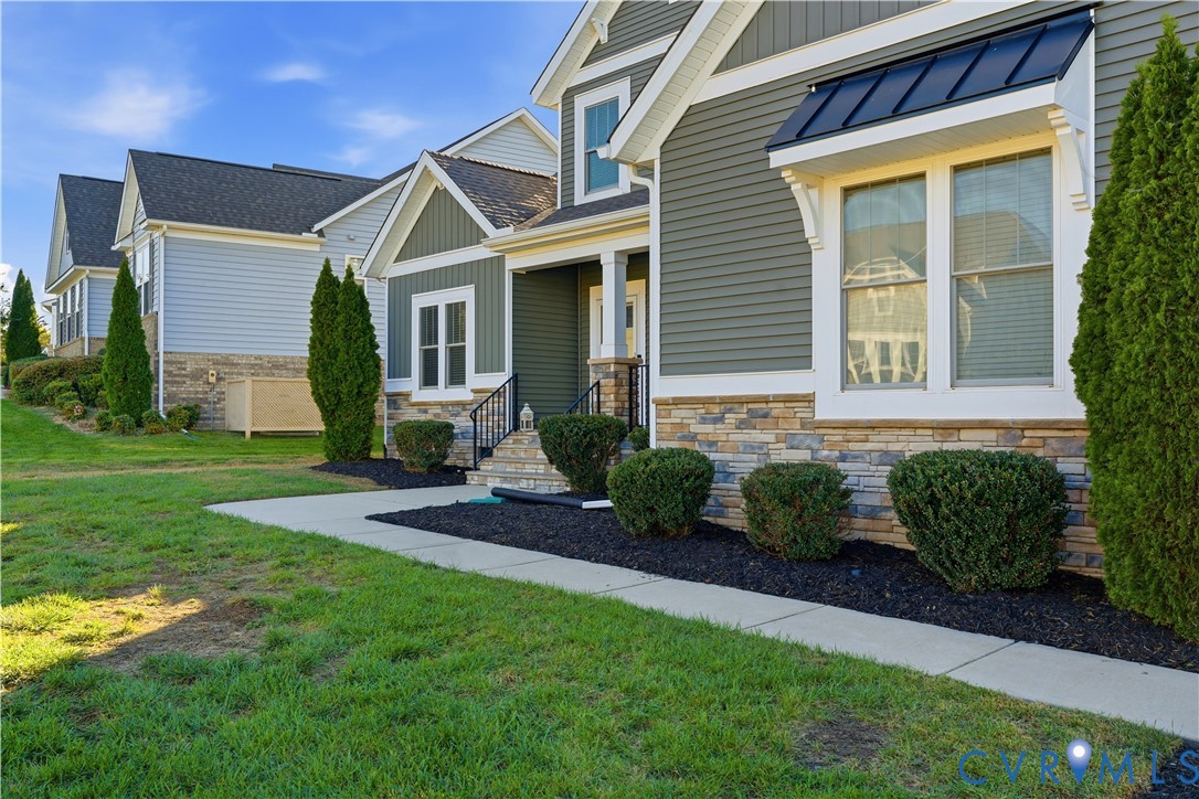 Exterior featuring horizontal lap siding, a stone veneer foundation, black metal roof awning, and multi-paned windows