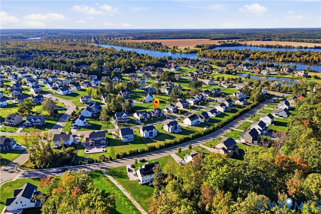Aerial perspective of the residential community featuring paved streets, landscaped lots, and proximity to expansive waterfront and wooded areas