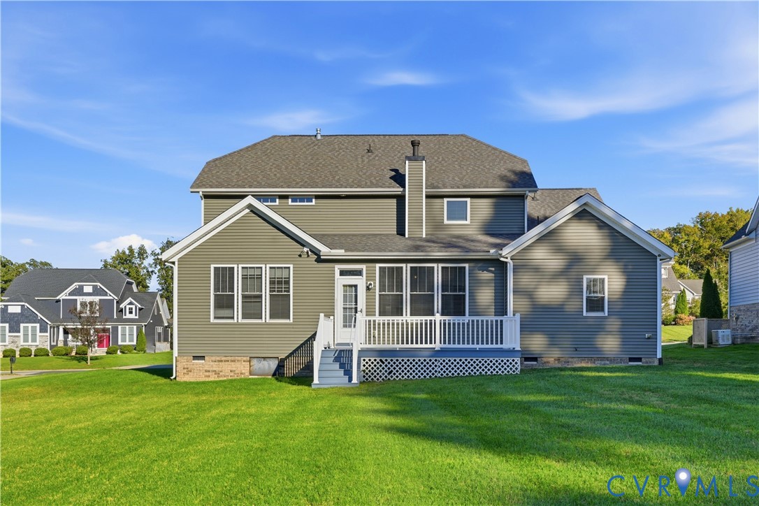 Rear exterior featuring gray horizontal siding, a central chimney, a raised deck with white railing, and a sprawling lawn