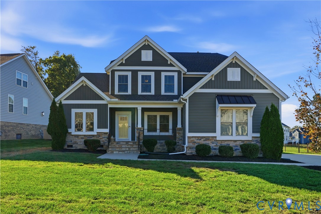 Two-story exterior featuring multi-textured horizontal and vertical siding, stone veneer base, metal window awning, and gabled rooflines