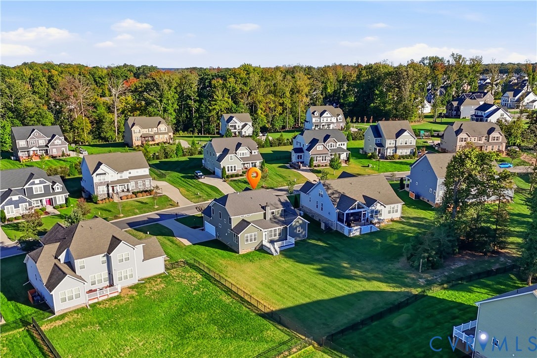 Aerial perspective of a multi-story residence featuring a shingled roof, attached garage, rear deck, and an expansive lawn with fencing