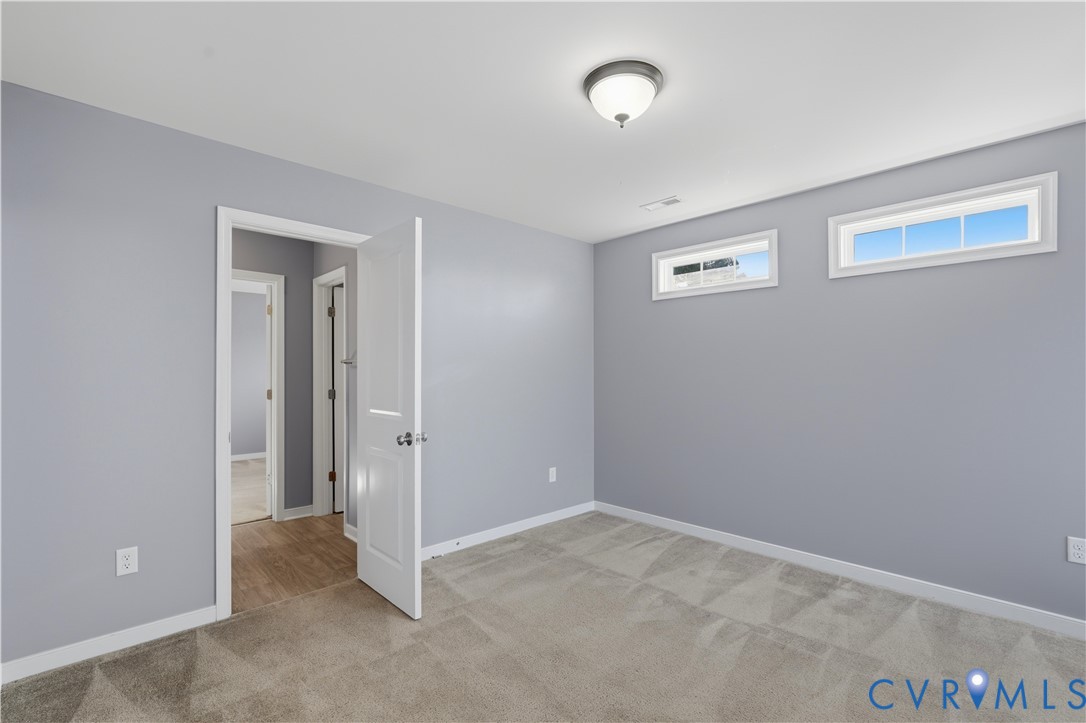 Bedroom #4 Neutral-toned interior space featuring light grey walls, wall-to-wall carpeting, two horizontal transom windows, and a classic flush-mount ceiling light fixture